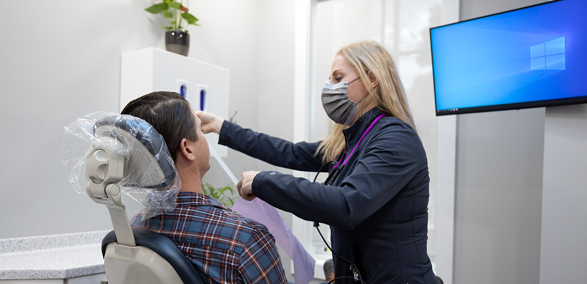 Female dentist putting a bib on a male patient sitting upright in dental chair