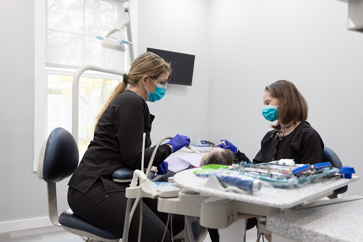 Two female dentists working on a patient laying back in a dental chair
