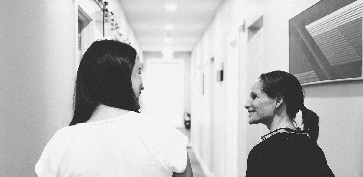 Black and white photo shot from behind of Dr. Aerwen Stagers and a patient smiling and talking in the Williston Road Family Dental office hallway