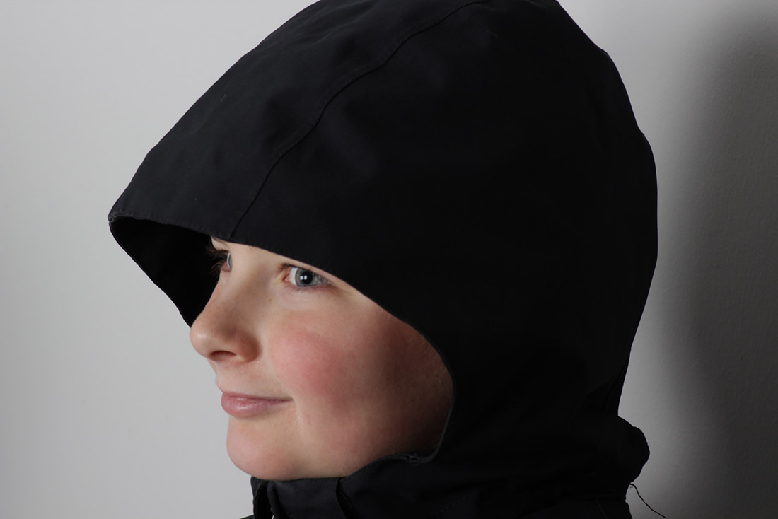 Angled headshot of young male patient named Keegan with black jacket hood over his head
